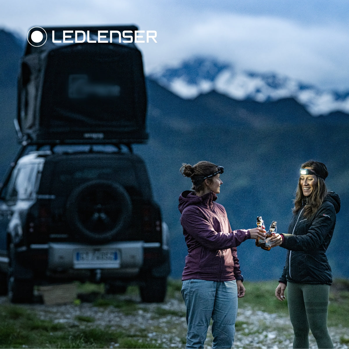 Two women on a mountain with drinks in hand wearing Ledlenser HF6R headtorches