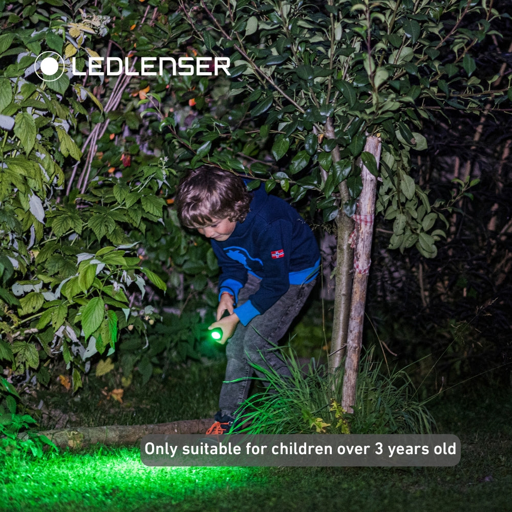 Child holding a green LED flashlight in a dark outdoor setting with LEDLENSER branding.