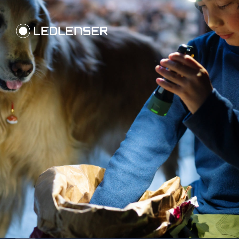 Child holding a flashlight with a dog in the background, featuring LEDLENSER branding.