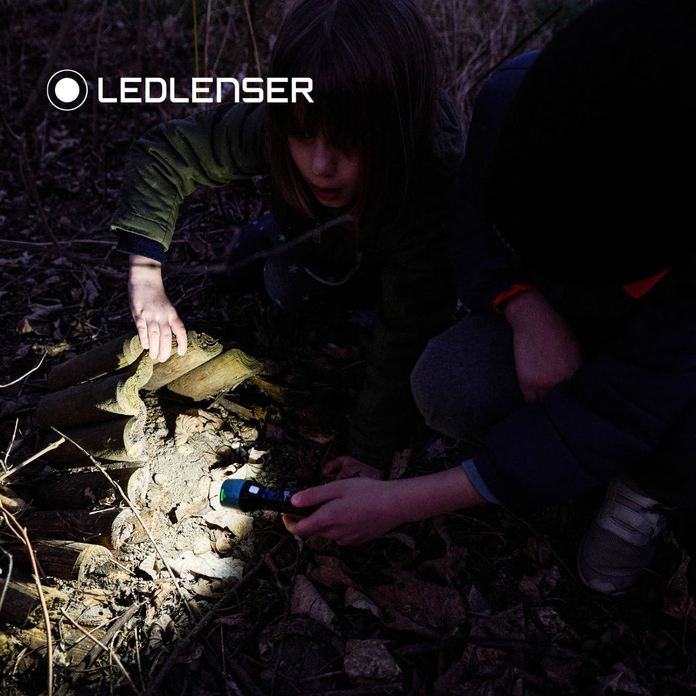 Child using a Ledlenser flashlight in a dark forest with Ledlenser logo.
