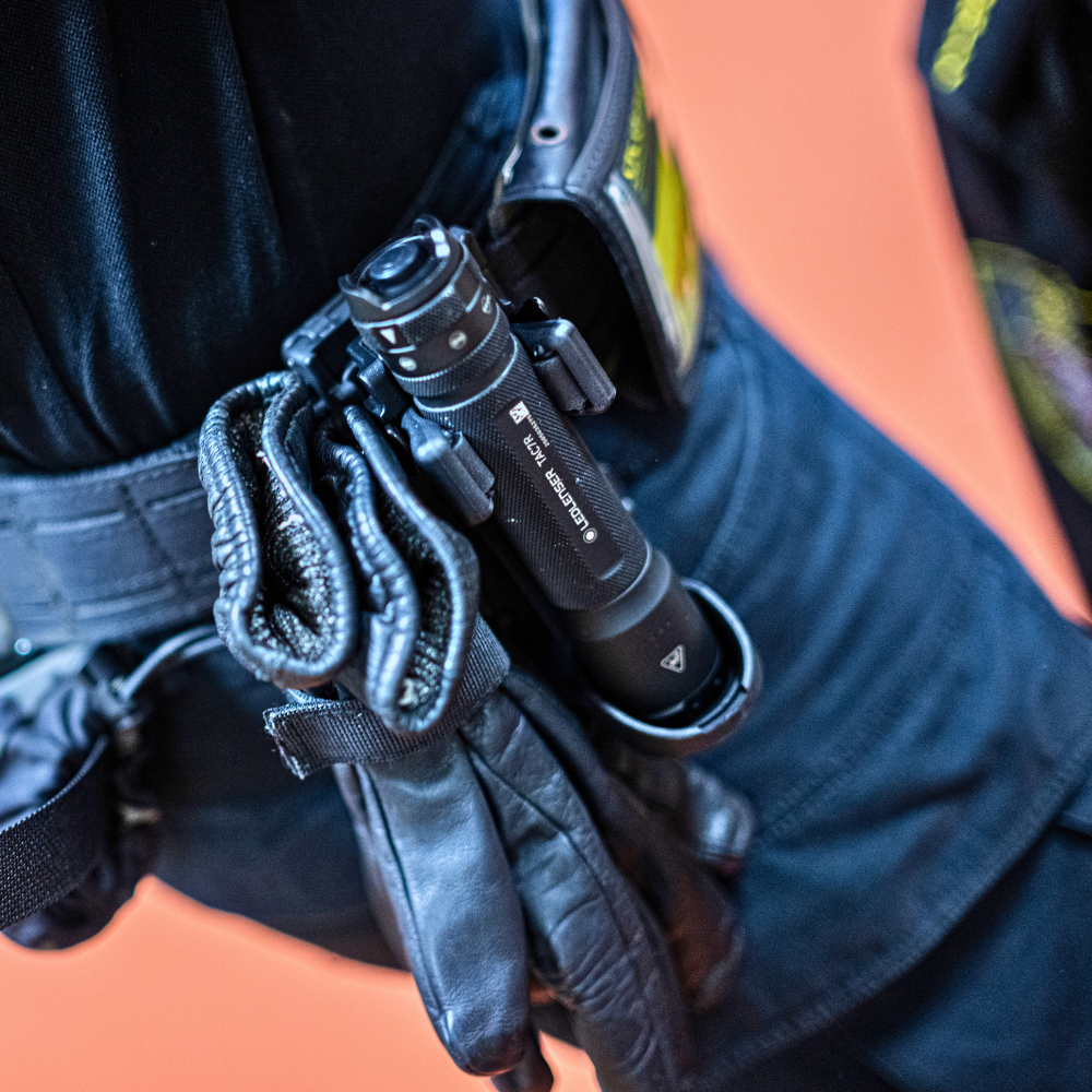Security holding a black TT3R torch with a strap, wearing a dark shirt and gloves.