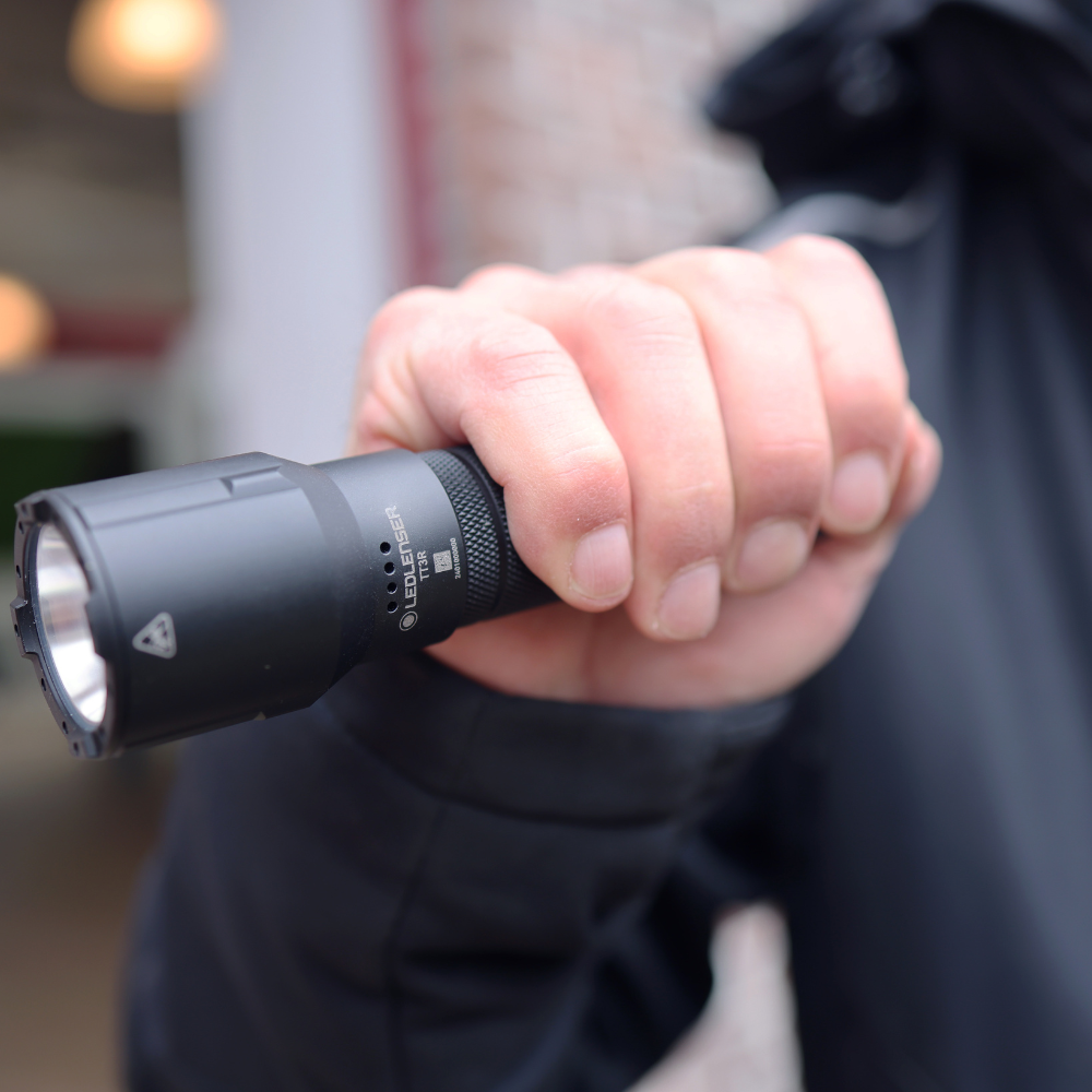 Hand holding a black TT3R torch with a blurred background